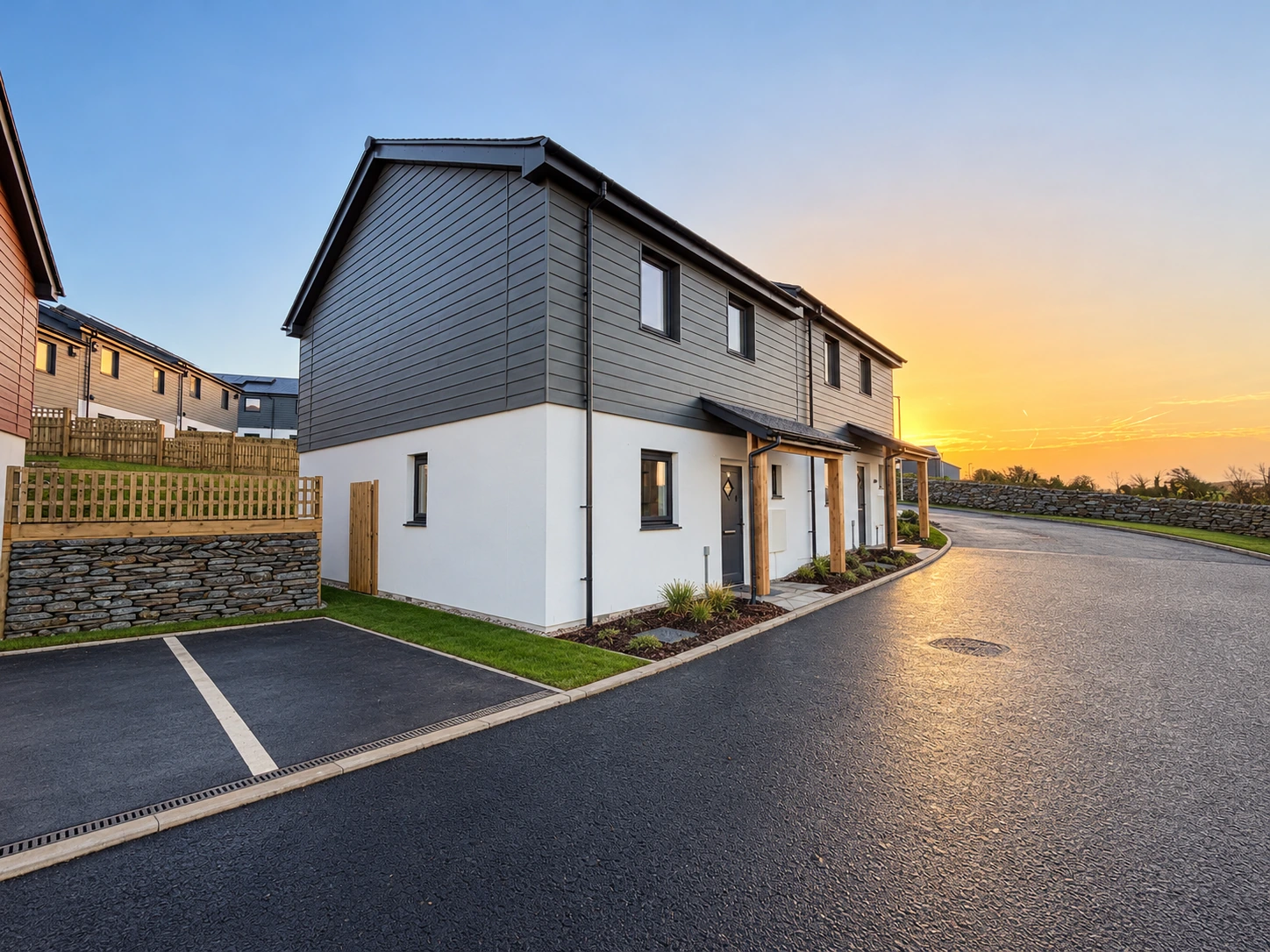 Grey-clad homes at Trevithick Manor Farm, Newquay, at sunset; site materials removed and landscaping digitally enhanced.